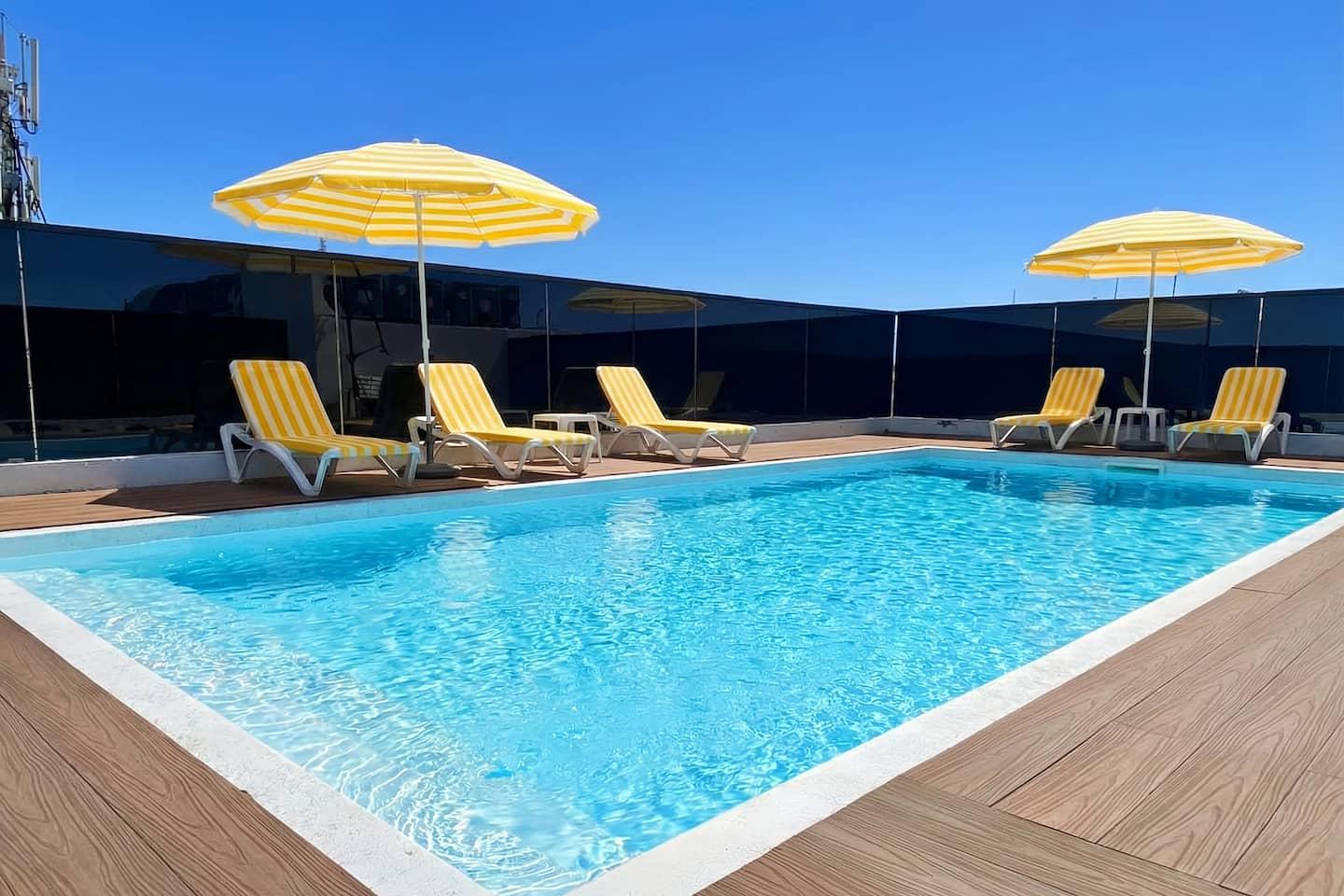Piscine sur le toit avec transats et parasols jaunes — Maya Suites